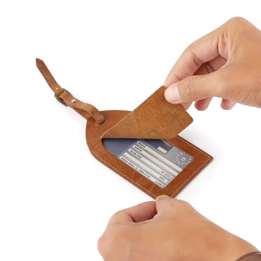 Top view of tan full-grain leather luggage tag showing ID window, flap cover, and buckle strap.