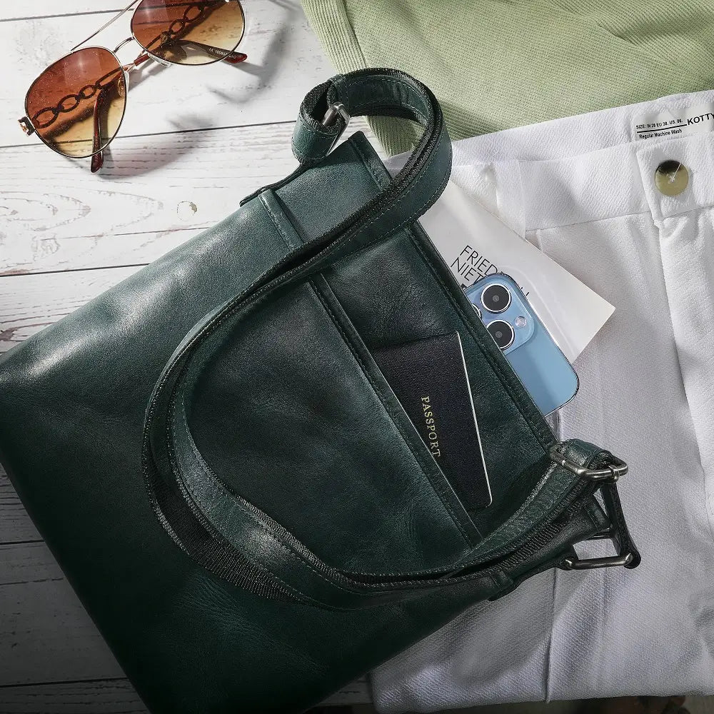 Teal leather bag with sunglasses and phone on a wooden surface