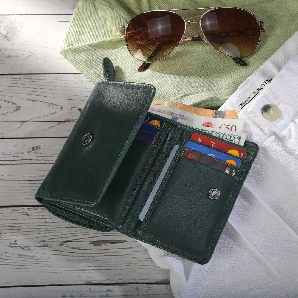 Open Teal wallet with money and cards on a wooden surface with sunglasses and a green shirt in the background.