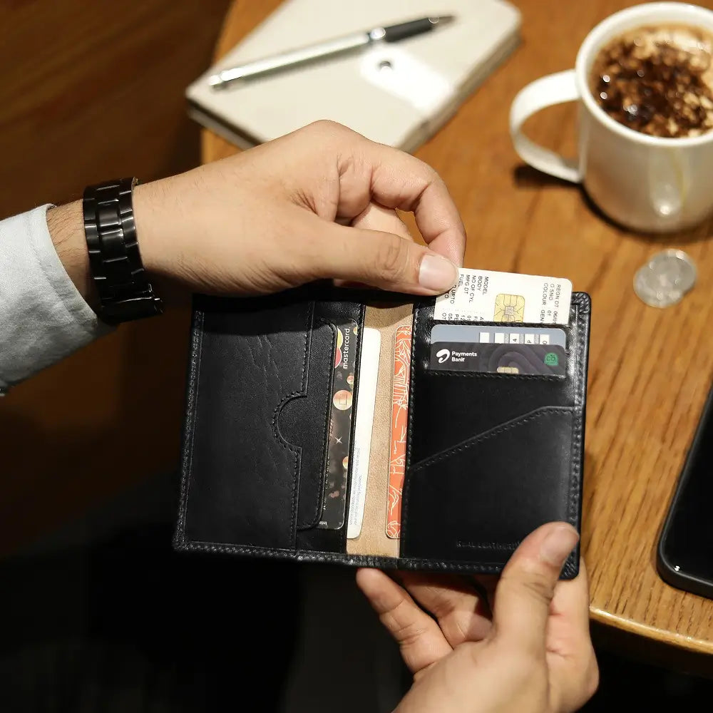 Person holding a black wallet with cards on a wooden table with a cup of coffee and phone.