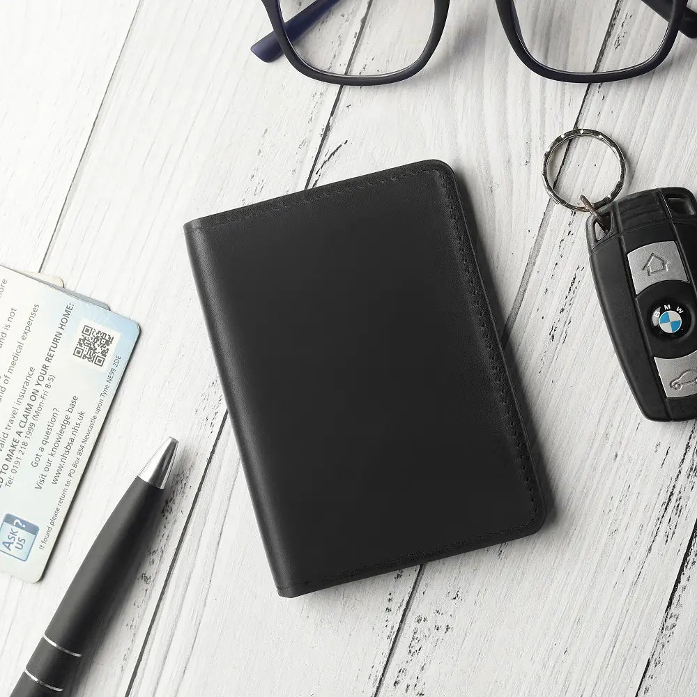 Black leather wallet with car keys, glasses, and a pen on a light wooden surface