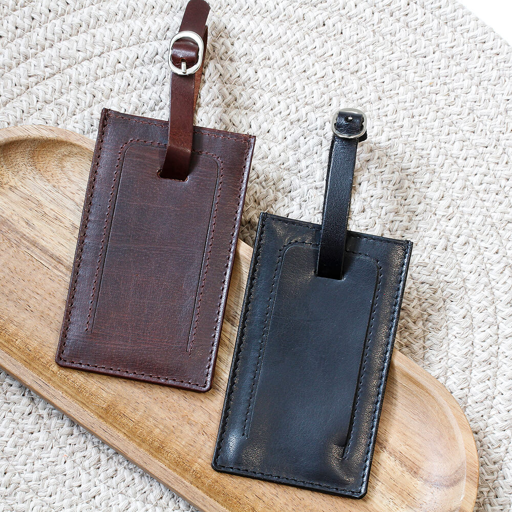 Two leather luggage tags, one brown and one black, on a wooden tray.