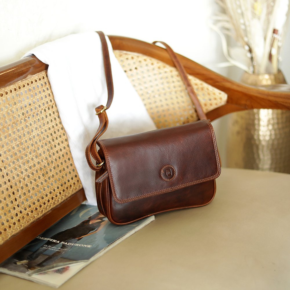 Orion brown leather handbag by Primehide resting on chair, showcasing flap-over design.