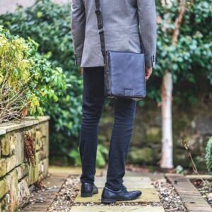 a man in a suit carrying a man bag in a crossbody style.