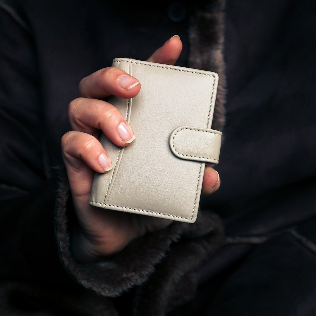 a woman is holding up a grey leather credit card holder with detailed stitching. the leather has a soft luxurious look