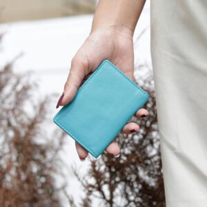 A hand holding the compact turquoise leather travel card holder, demonstrating its portable size and practicality for everyday use or travel.