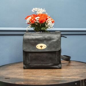 a black leather handbag with a brass twist lock is sitting on a wood table