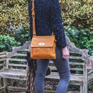 a woman is wearing a large yellow leather handbag in a crossbody style. The handbag has a long leather strap with brass buckle adjusters