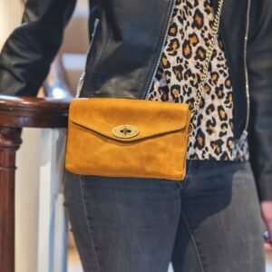 a women in a black leather jacket with a small yellow leather crossbody bag. the bag has a brass coloured metal chain