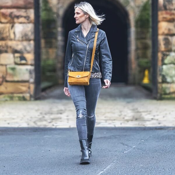 a woman is walking down a street wearing a fashionable black leather jacket and a medium yellow leather handbag