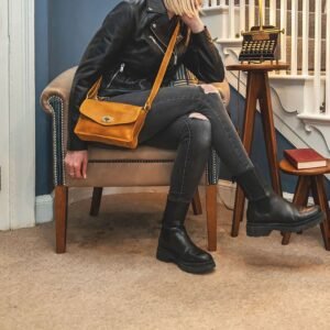 a woman is sitting on a chair and is wearing a biker style leather jacket and a yellow leather crossbody handbag