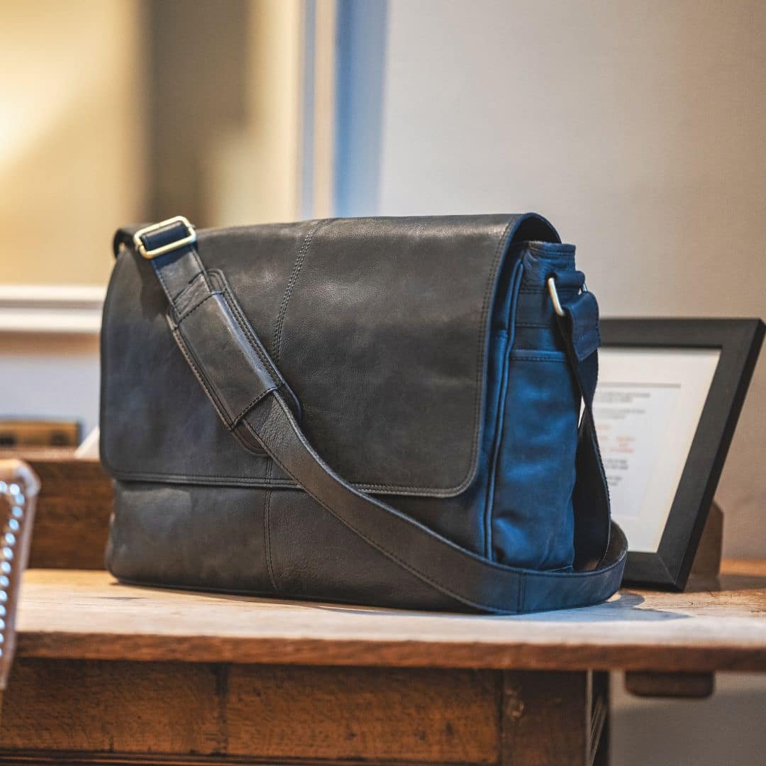 a black leather messenger bag for men with a leather strap that has a metal adjuster and shoulder pad