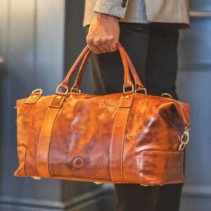 A gentleman is elegantly grasping a sizeable luxury leather holdall in a rich shade of brown.