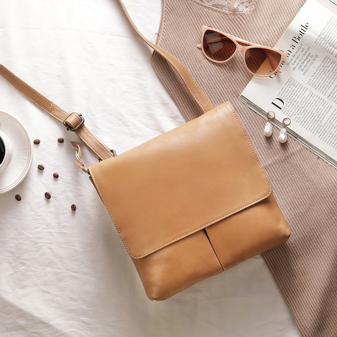 A sand-coloured PRIMEHIDE crossbody organiser bag made of real leather laid out on a white surface with a magazine, sunglasses, a cup of coffee, and other small items.