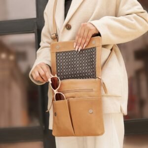 A person wearing a beige coat holds open the sand-coloured PRIMEHIDE crossbody organiser bag made of real leather, showing its patterned lining and compartments with sunglasses inside.