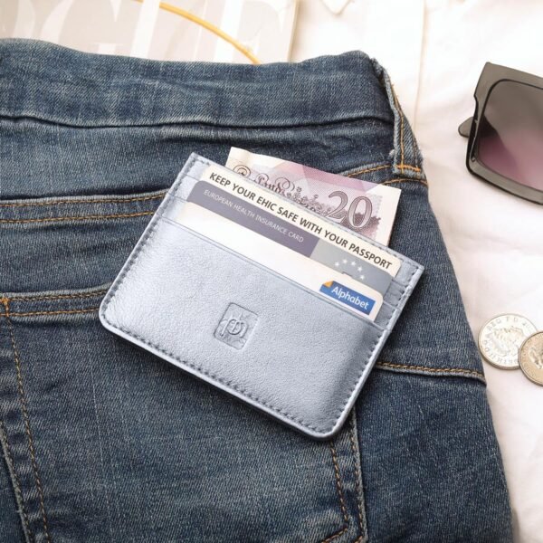 Silver personalised leather card holder filled with cash and cards, styled on a pair of blue jeans alongside sunglasses and coins.