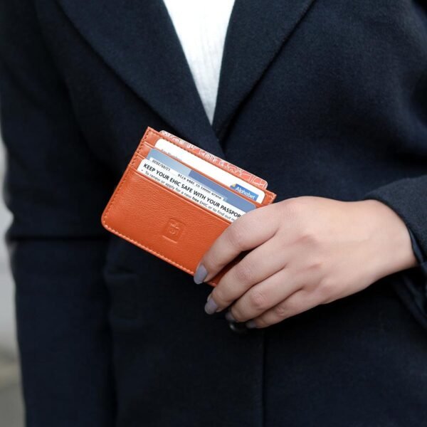 Woman holding a tan leather RFID card holder while wearing a black coat.